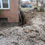 Excavation site showing foundation repair work near a residential home in Perrysburg, Ohio, with visible dirt piles and structural support in place.