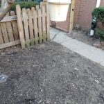 Image of a cleared area near a house, featuring a wooden fence, sidewalk, and a tree, illustrating the site of foundation repair work related to basement waterproofing and structural issues addressed by Toledo Basement Repair.