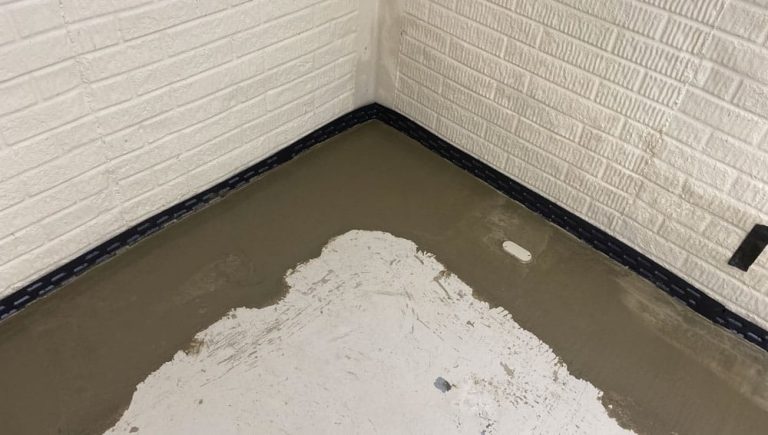A corner of a room with textured white brick walls shows partial flooring under construction. Smooth concrete edges surround an uneven white surface.