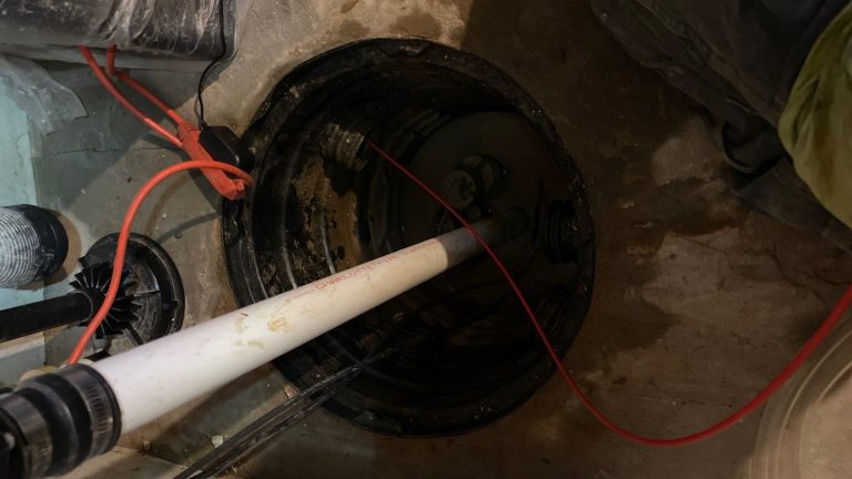 Sump pump installation in a basement, showcasing a pipe and water level, relevant to basement waterproofing and moisture management in Toledo.
